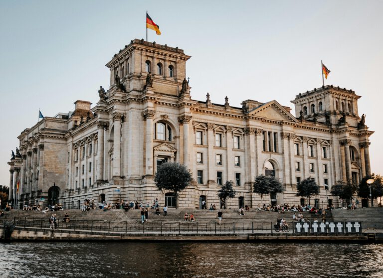 Photo of the Reichstag building in Berlin, Germany with a riverside view at sunset.